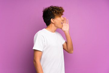 Young african american man over isolated purple wall shouting with mouth wide open to the lateral