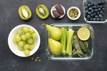 Healthy food fresh ingredients vegetables fruit berries seeds. Glass containers for lunch with juicy celery, lime, lettuce, sorrel, kiwi, grapes...