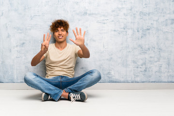 Young african american man sitting on the floor counting eight with fingers