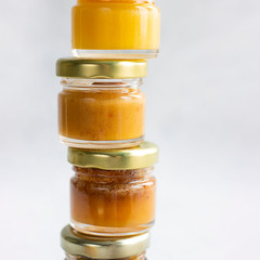 Five Small glass jar with metal cap with different kinds and colours of honey one on another isolate, on the edge of grey cement background, copy space. Healthy product, natural Square
