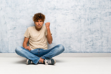 Young african american man sitting on the floor with angry gesture