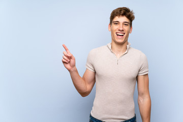 Handsome young man over isolated blue wall surprised and pointing side