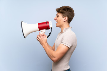 Handsome young man over isolated blue wall shouting through a megaphone