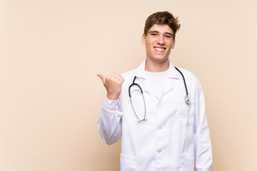 Handsome doctor young man over isolated wall pointing to the side to present a product