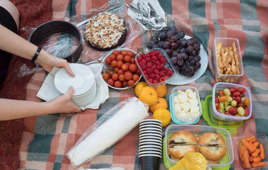 woman hand serving cake on picnic table with food served outdoors on the fabric picnic cloth. Close...