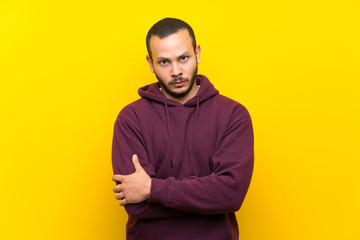 Colombian man with sweatshirt over yellow wall feeling upset