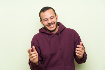 Colombian man with sweatshirt over green wall laughing