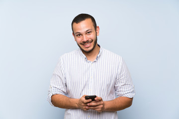 Colombian man over isolated blue wall sending a message with the mobile