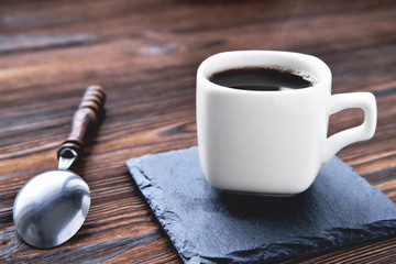 white cup with coffee on a stone stand, vintage coffee spoon, wooden natural background close up