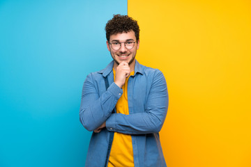 Fototapeta premium Man with curly hair over colorful wall with glasses and smiling