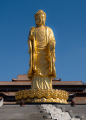 Golden metalic style giant buddha statue with temple roof and blue sky on background, Urumqi, China