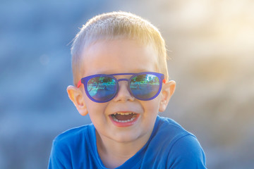 Young white preschool 4 years old boy in sunglasses happily laughing while looking at the camera on a sunny summer day