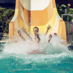 Mother and son having fun on the water slide in the aqua fun park glides, happy falling into water and water splashes are all over. - 278237619