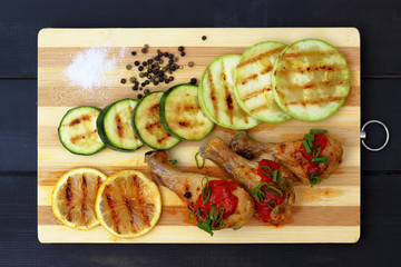 grilled chicken, tomato sauce and zucchini on a wooden board, black background