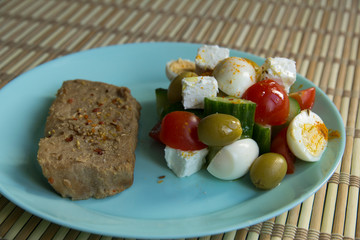 Piece of pork, tomato salad, cucumber, pickle cheese, olives, quail eggs
