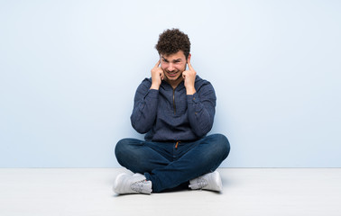 Young man sitting on the floor frustrated and covering ears