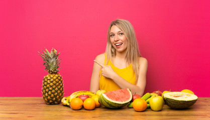 Young blonde woman with lots of fruits pointing finger to the side