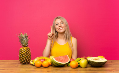 Obraz premium Young blonde woman with lots of fruits pointing with the index finger a great idea