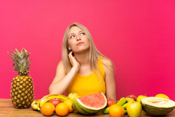 Young blonde woman with lots of fruits thinking an idea