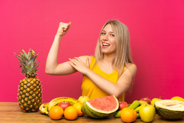 Obraz premium Young blonde woman with lots of fruits making strong gesture