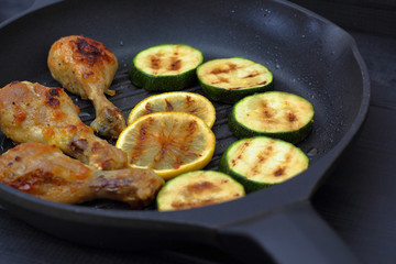 grilled chicken, tomato sauce and zucchini on a griddle, black background
