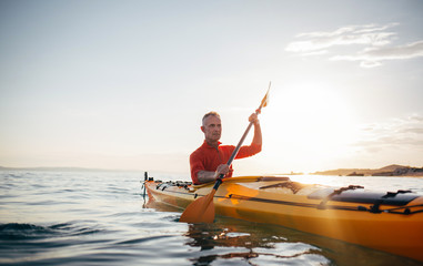 Senior man paddling kayak on the sunset sea - obrazy, fototapety, plakaty