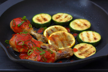 grilled chicken, tomato sauce and zucchini on a griddle, black background