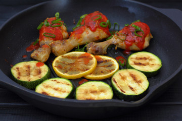 grilled chicken, tomato sauce and zucchini on a griddle, black background