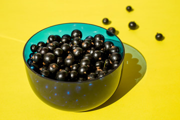 Black currant berries in a glass plate on a yellow background.
