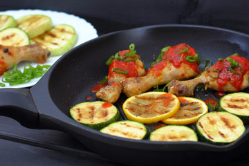 grilled chicken, tomato sauce and zucchini on a griddle, black background