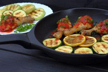grilled chicken, tomato sauce and zucchini on a plate, black background