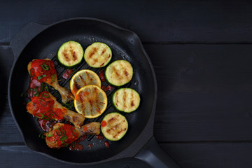 grilled chicken, tomato sauce and zucchini on a griddle, black background