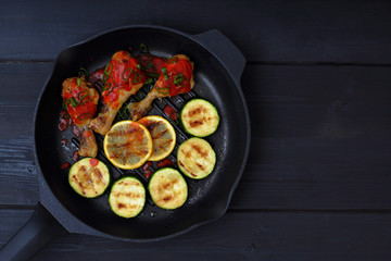grilled chicken, tomato sauce and zucchini on a griddle, black background
