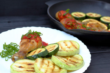 grilled chicken, tomato sauce and zucchini on a plate, black background