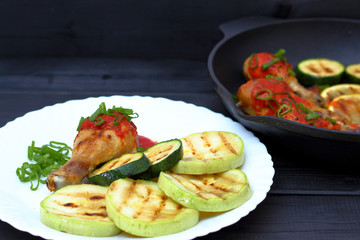 grilled chicken, tomato sauce and zucchini on a plate, black background