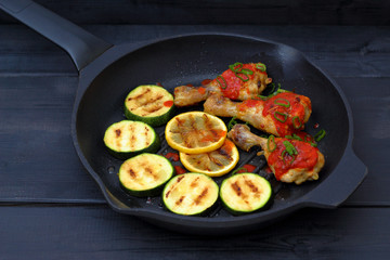 grilled chicken, tomato sauce and zucchini on a griddle, black background