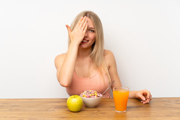 Young blonde woman having breakfast covering a eye by hand