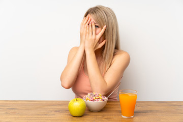 Young blonde woman having breakfast covering eyes and looking through fingers