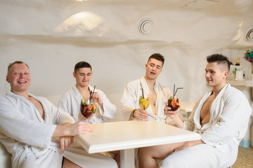 close up photo of 4 men in white gowns sitting around a table and drinking sangria and limonade