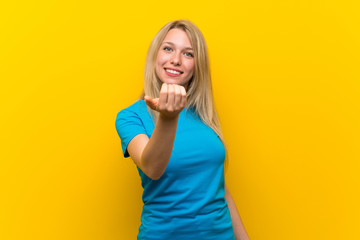 Young blonde woman over isolated yellow background inviting to come with hand. Happy that you came