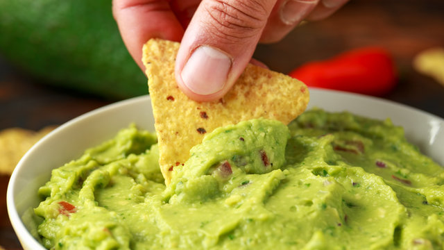 Man hand is picking some guacamole dip with nachos chip. Healthy Vegan, Vegetables food.