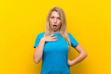 Young blonde woman over isolated yellow background surprised and shocked while looking right
