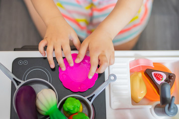 Little girl chef cooking in toy kitchen. Kids play and cook at home or daycare. Toddler kid playing with toy vegetables and dishes.