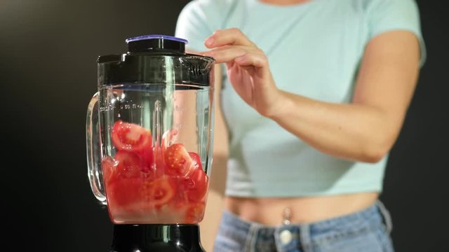 A young woman puts tomatoes in to the blender and turns it on . Close up