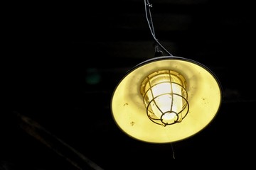 A yellow vintage light lamp hanging from the building ceiling and glowing in the dark night scene 