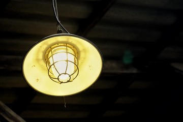 A yellow vintage light lamp hanging from the building ceiling and glowing in the dark night scene 