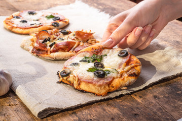Traditional Italian appetizer - a woman takes a mini pizza, pizzetta with sausage, olives and mozzarella cheese, close-up of a hand with a pizza - obrazy, fototapety, plakaty