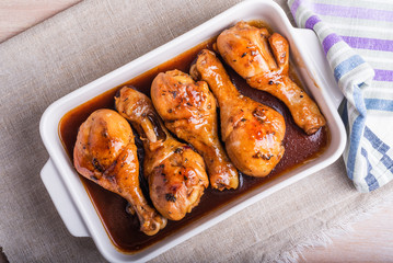 Chicken drumstick baked in sweet soy sauce in white ceramic baking dish.