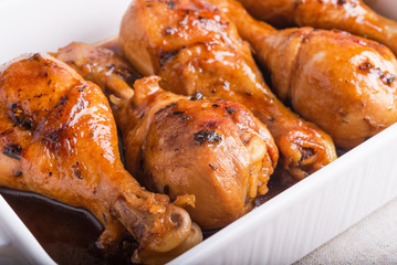 Chicken drumstick baked in sweet soy sauce in white ceramic baking dish, close-up.