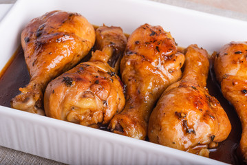 Chicken drumstick baked in sweet soy sauce in white ceramic baking dish, close-up.